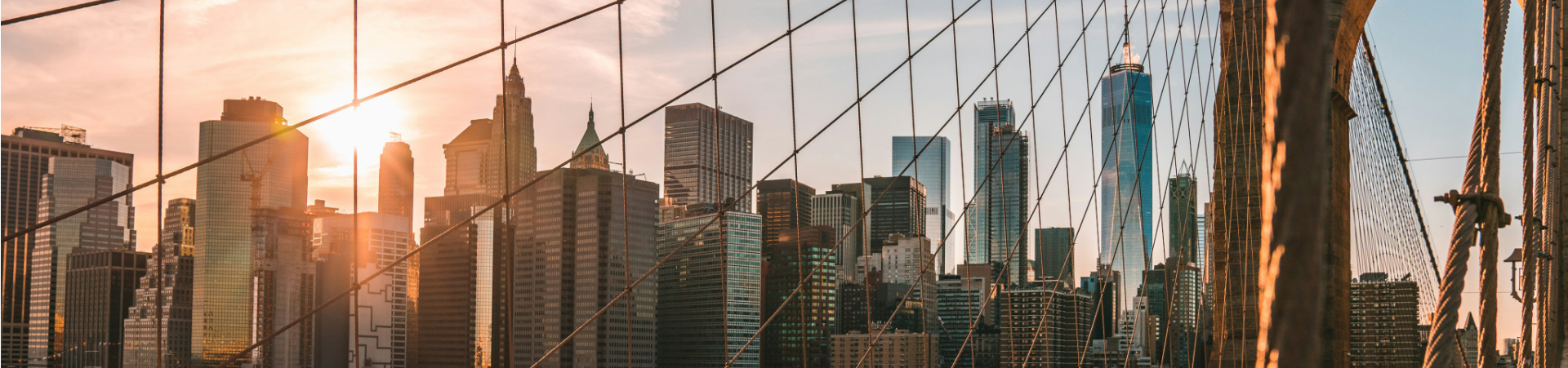New York city skyline as seen from a bridge with the sun rising in the background